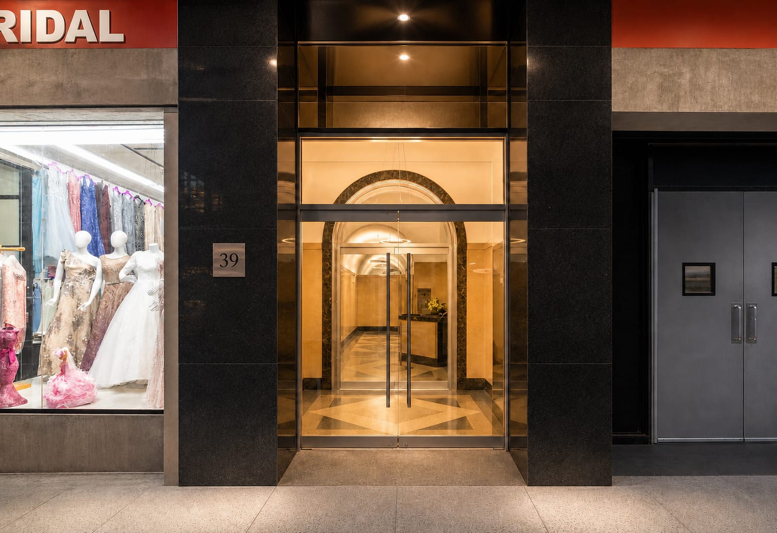 Street-level entrance: double glass doors framed by dark polished stone pillars, lobby visible through the glass